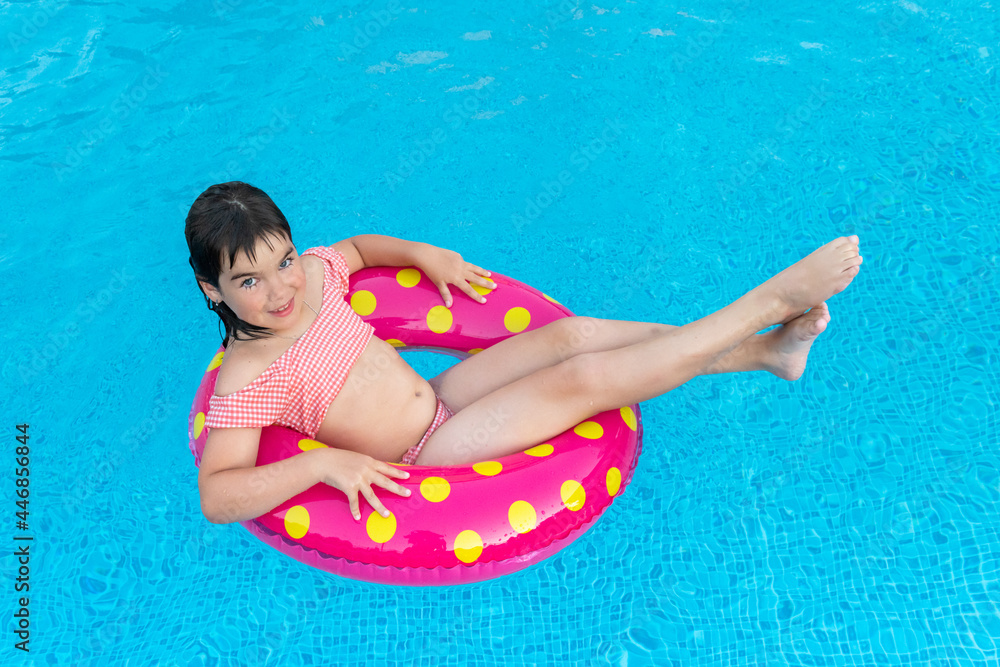 cute smiling girl in a bright circle swims on the background of a blue pool in summer. High quality photo