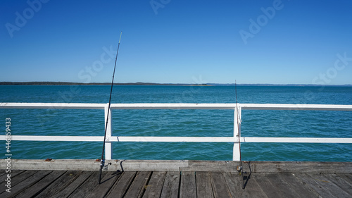Fishing rods leaning on the white handrails of the jetty against a background of blue sea and sky