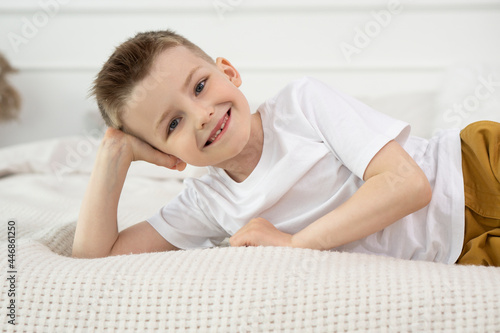 Happy Child boy smiling and looking into the camera while lying on his side in bed. Kid Boy close-up on a white background, looking into the camera.