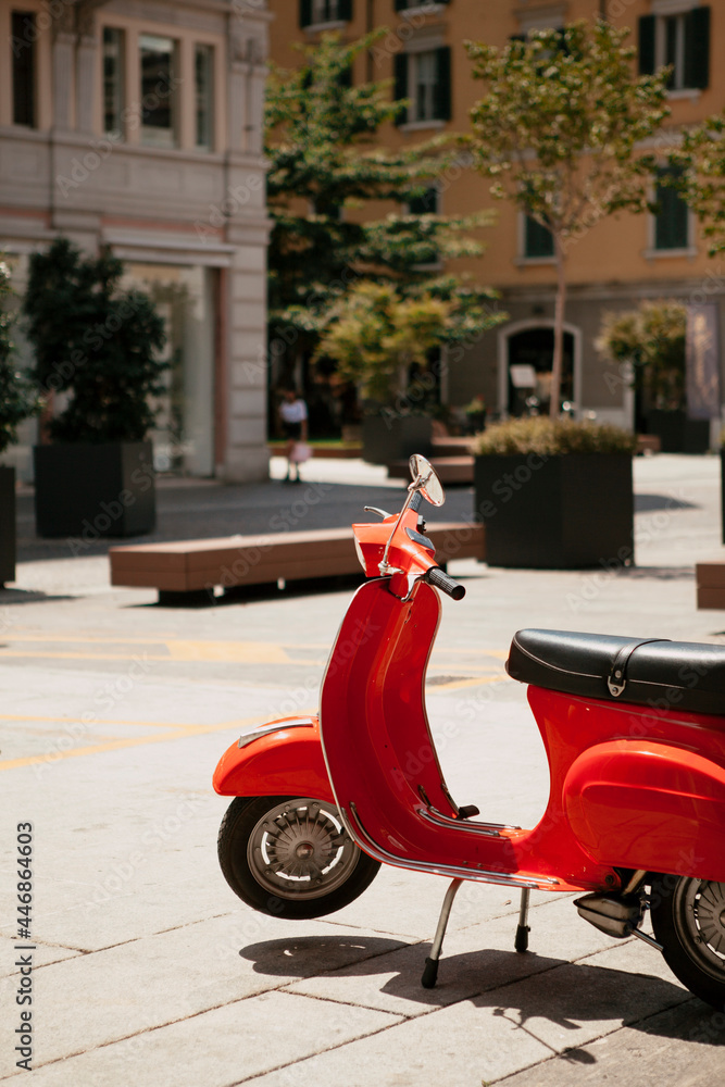 Close up. The Italian red scooter parked on a narrow Italian public street in the city center of Brescia, Lombardy, Italy. European traditional vehicle (motorcycle) outside on a sunny day.