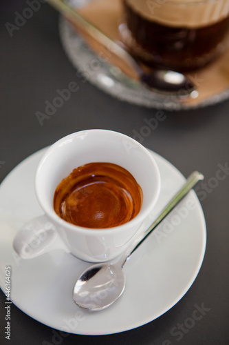 Traditional Italian coffee. The white small espresso cups on a white saucer with a spoon on a black table at the bar (coffeeshop) in Milan, Lombardy, Italy. European beverages and drinks. 
