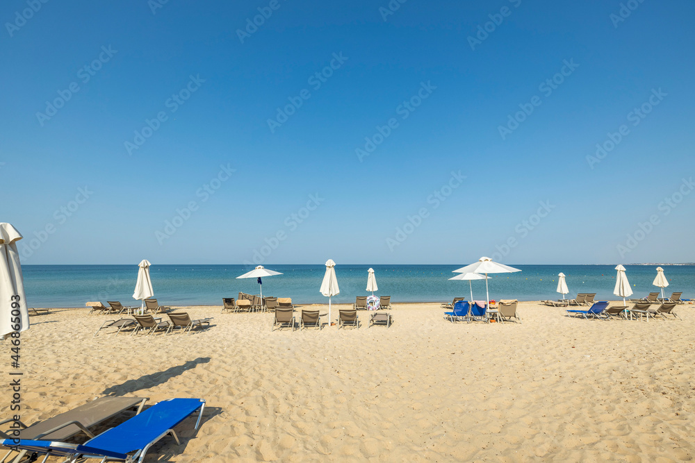 Landscape view of empty sunbeds under umbrellas on sand beach. Greece. 