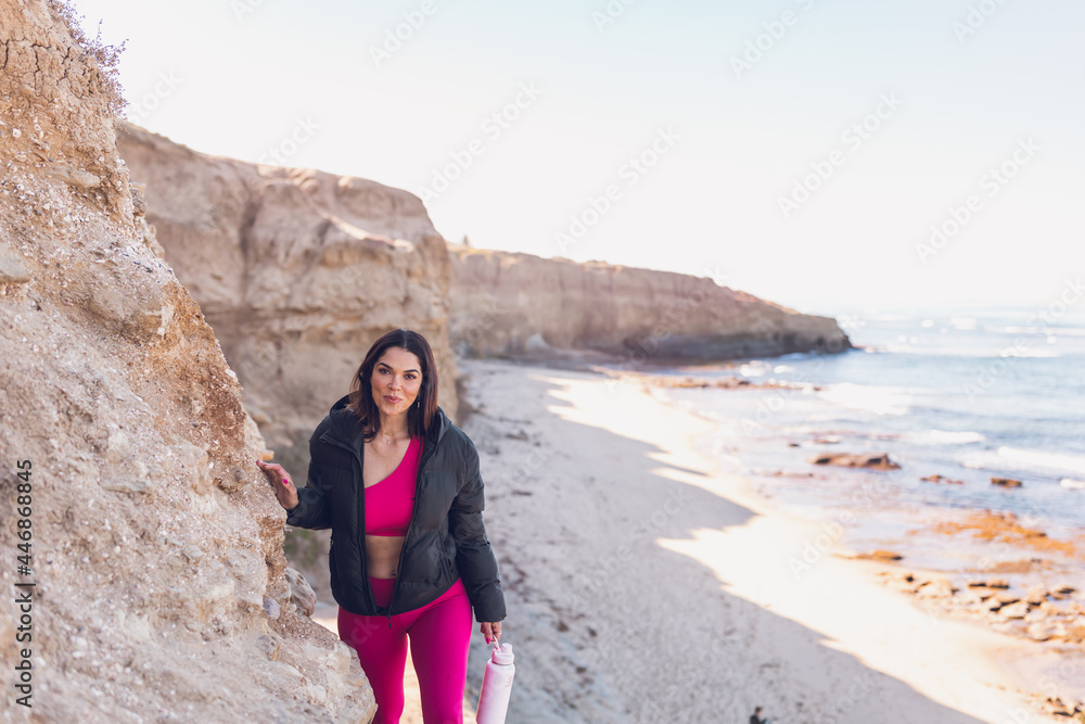 Woman wearing gym clothes walking on the beach cliffs in California.