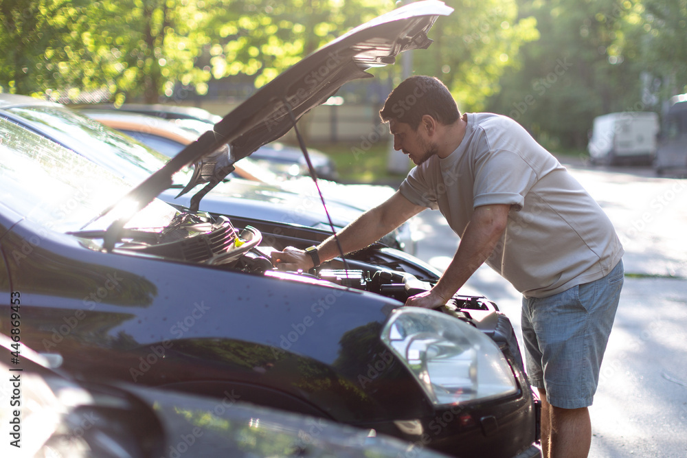 a man on a city street checks the operation of the car, looks under th a man on a city street checks the operation of the car, looks under th
