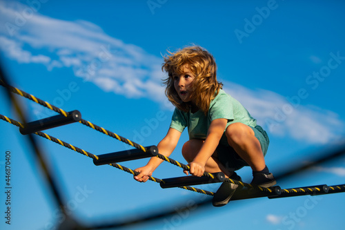 Cute boy climbs up the ladder on the playground. Child climbs up the ladder against the blue sky. Young boy exercise out playground.