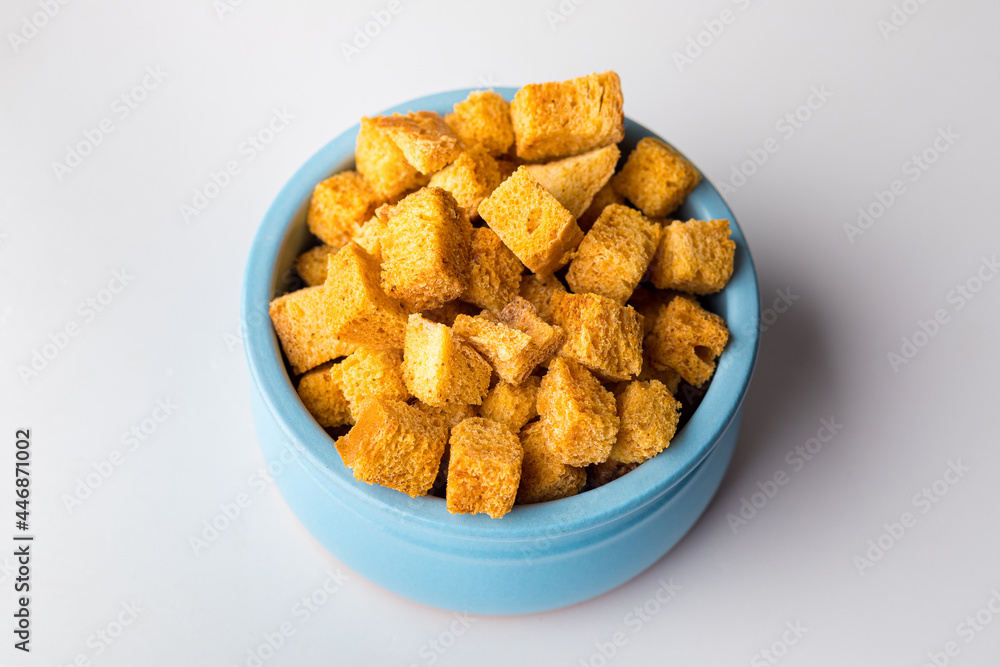 Square-shaped bread crumbs in a blue pot on a white background. Oven-fried golden brown bread crumbs. Close-up. Square-shaped bread crumbs in a blue pot on a white background. Oven-fried golden brown bread crumbs. Close-up.