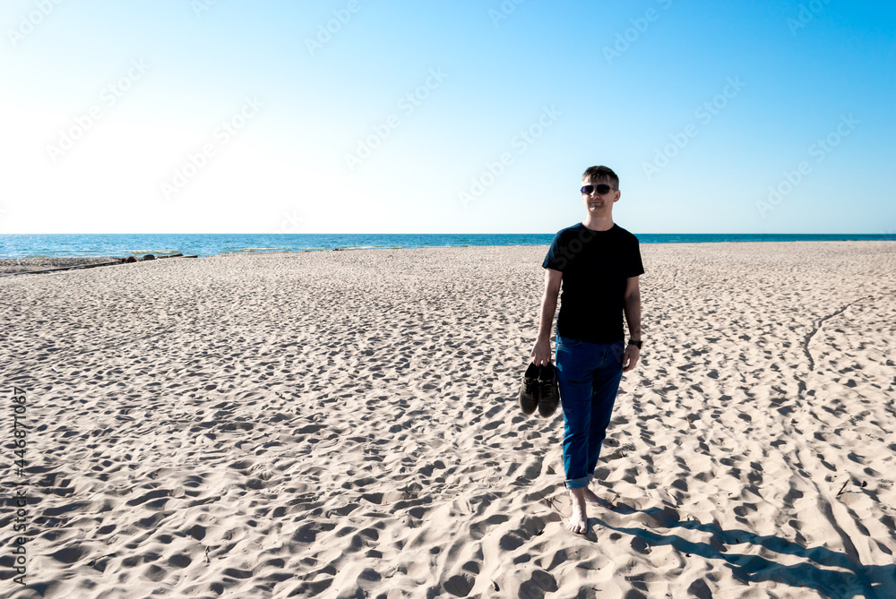 Man at afternoon on a deserted beach holds shoes in his hands