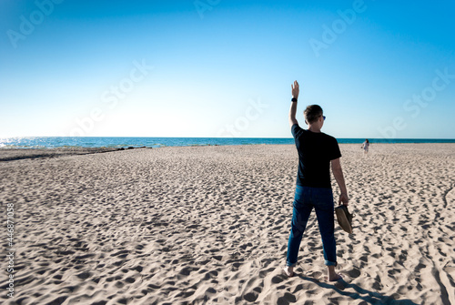 Man on the beach waves his hand to a woman walking in the distance