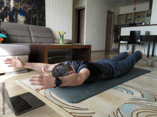 A man does yoga online at home on a gymnastics mat photo