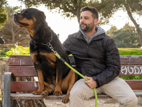 Man sitting on a park bench next to his rottweiler dog