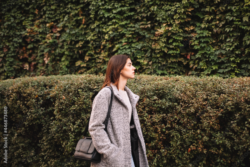 Young woman walking in city against green plants Young woman walking in city against green plants