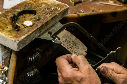 Men's hands in a jewelry workshop cutting piece of gold with hacksaw
