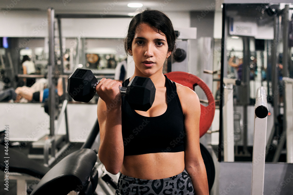 Young woman lifts weights in a gym looking at camera Young woman lifts weights in a gym looking at camera