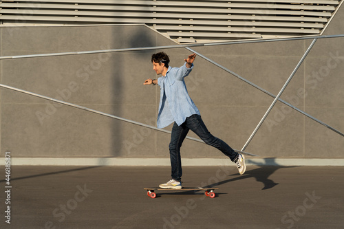 Man riding longboard perform tricks on skateboard in urban street skatepark. Casual hipster guy wearing jeans shirt and bandana skateboarding. Leisure activity, sport extreme, city lifestyle concept © DimaBerlin