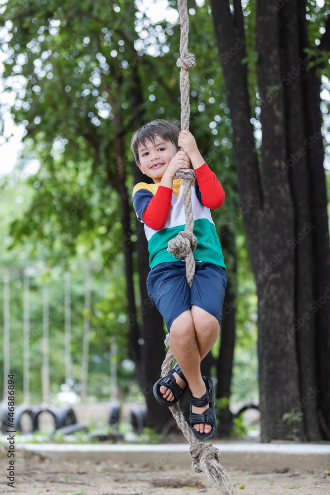 A boy wearing bright colored clothes playing rope hanging at playground and having fun healthy summer vacation activity.The concept of healthy lifestyle