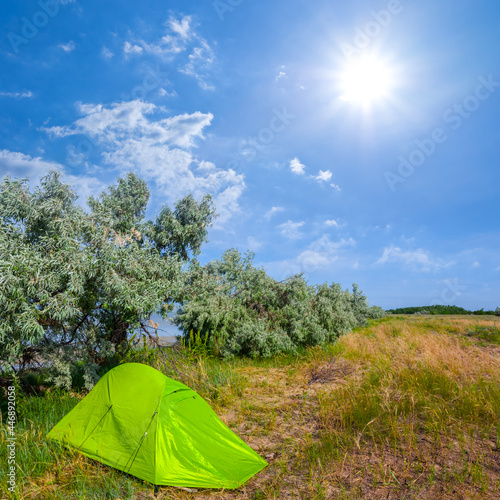 green touristc tent stay on forest glade under a sparkle sun, natural travel background photo