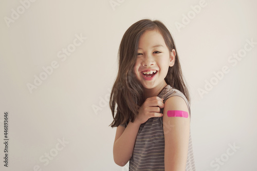 Foto Mixed Asian young girl showing her arm with pink bandage after got vaccinated or