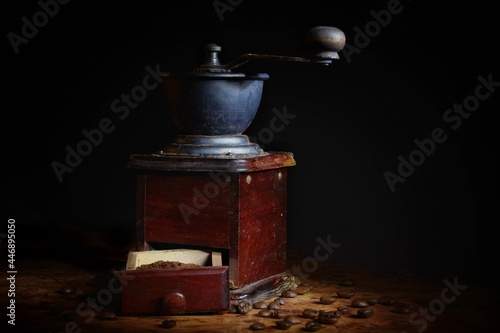 an old coffee grinder with an extended drawer and coffee beans lying next to it on a black background
