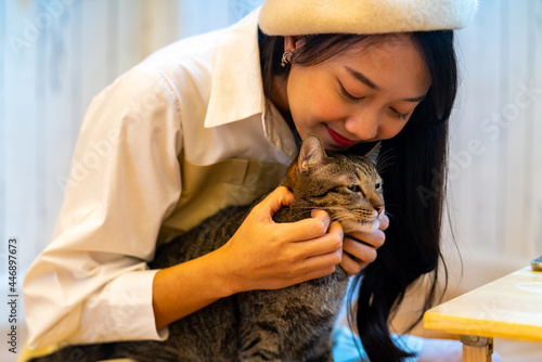 Young Asian woman sitting on floor playing and stroking adorable cat with happiness. Pretty girl enjoy indoor lifestyle with friendly cat at home. Pet and owner friendship and relationship concept