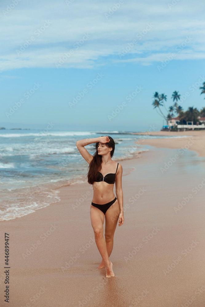 Beautiful woman in swimwear with copy space on the beach. Portrait of pretty girl with slim tanned sexy body in black bikini enjoying life. Summer lifestyle. Vacation