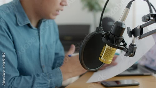 Asian male podcaster recording and broadcasting her podcast from home. Man working from home at night reading a notepad, paper work and talking into a microphone. photo