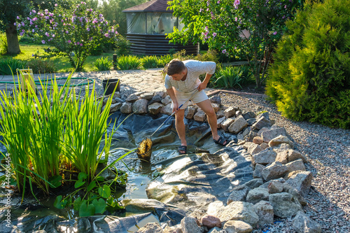 Man cleans garden pond bottom landing net from mud, sludge and water plants