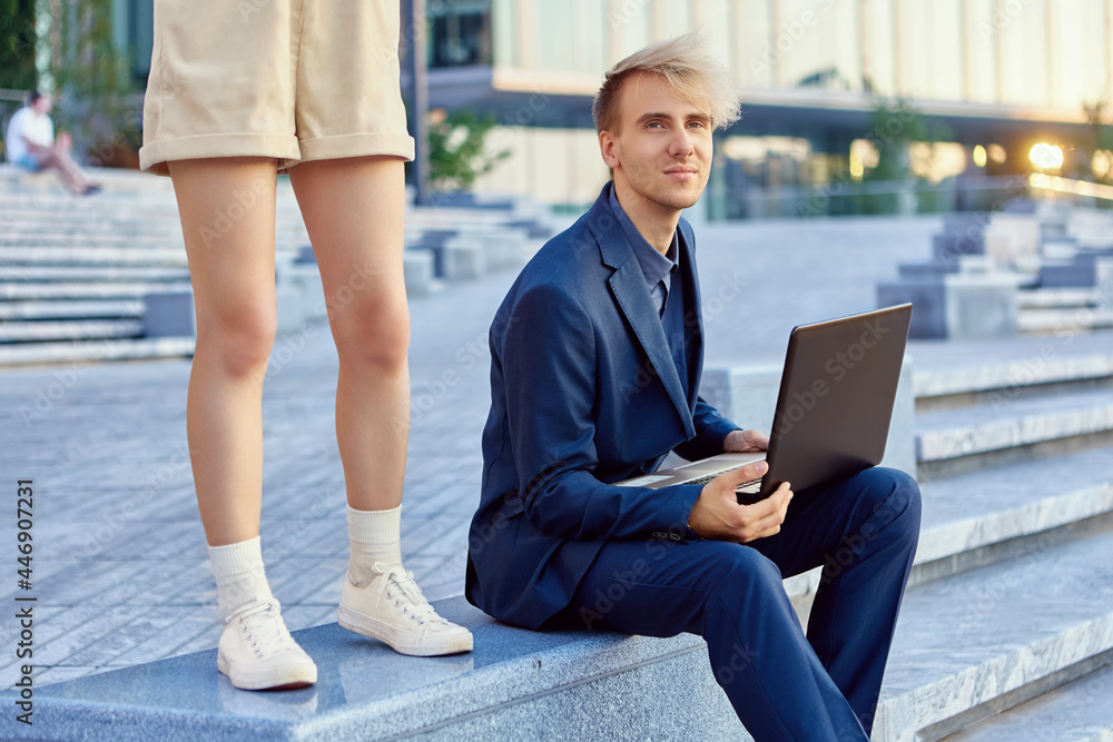 Man with notebook sits on stairs outdoors and woman stands near. Man with notebook sits on stairs outdoors and woman stands near.