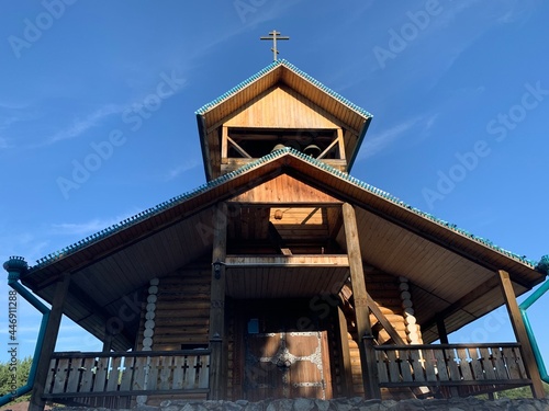 Old wooden church with walls and roof covered with wooden shingles, summer day.  © Никита Родионов