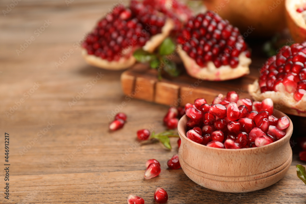Delicious ripe pomegranate kernels in bowl on wooden table. Space for text Delicious ripe pomegranate kernels in bowl on wooden table. Space for text