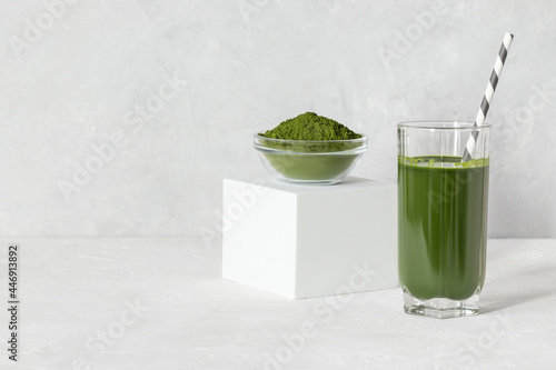 Green drink with chlorella in a glass and powder on a white concrete background. Healthy detox drink. Superfood concept. Copy space.