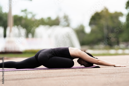 A confident middle-aged Asian woman in sports outfit doing yoga exercise on the yoga mat outdoor in the backyard in the morning. Young woman doing yoga exercise outdoor in nature public park