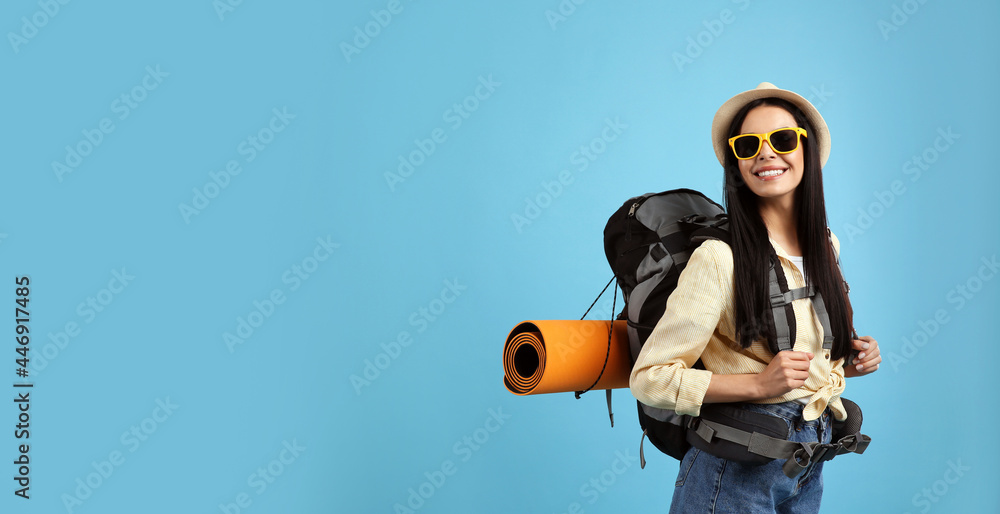 Obraz premium Happy female tourist with backpack on light blue background. Space for text