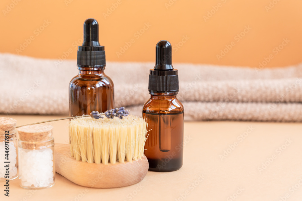 Dark glass bottle with essential oils, sea salt and face brush with natural bristle on beige background. Skin care concept with copy space. Natural cosmetics Dark glass bottle with essential oils, sea salt and face brush with natural bristle on beige background. Skin care concept with copy space. Natural cosmetics