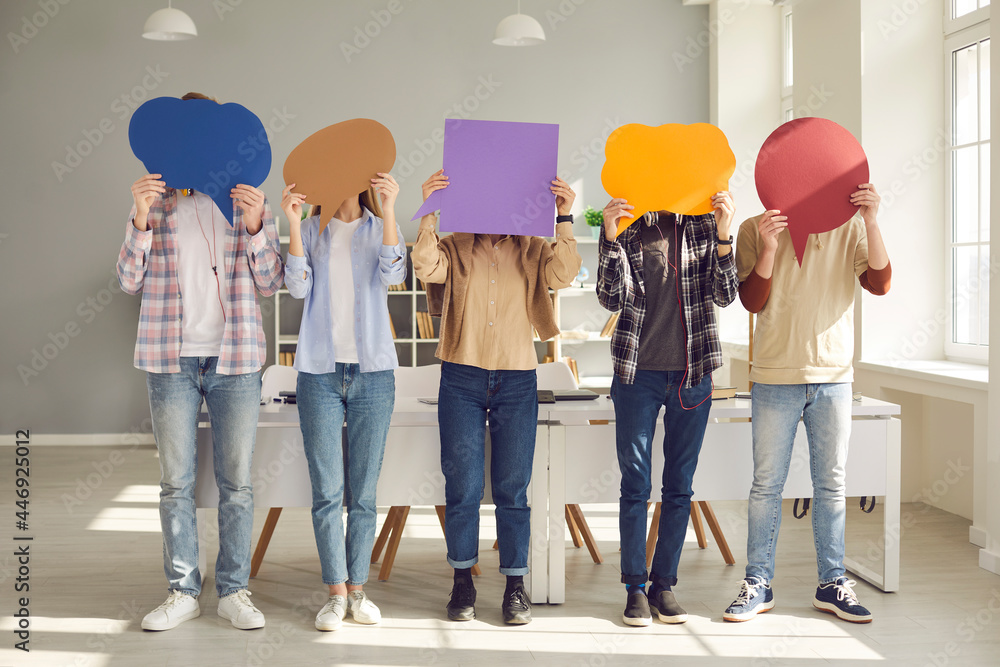 Obraz premium Faceless people sharing message or expressing opinion in anonymous survey. Group of unrecognizable young college or university students covering faces with multicolored paper mockup speech bubbles