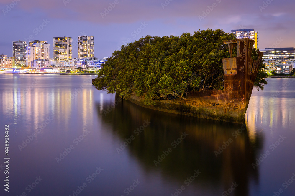 Shipwreck on river with cityscape long exposure