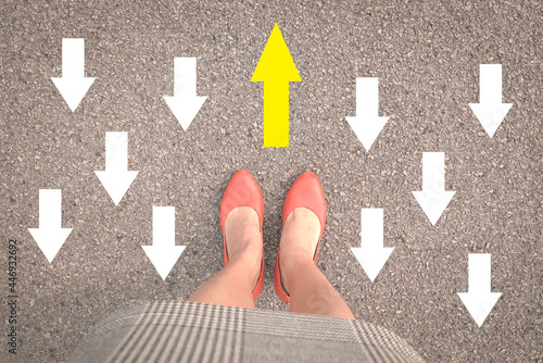 Fotografia Businesswoman standing with orange shoes on street with one yellow arrow against other opposing direction white arrows