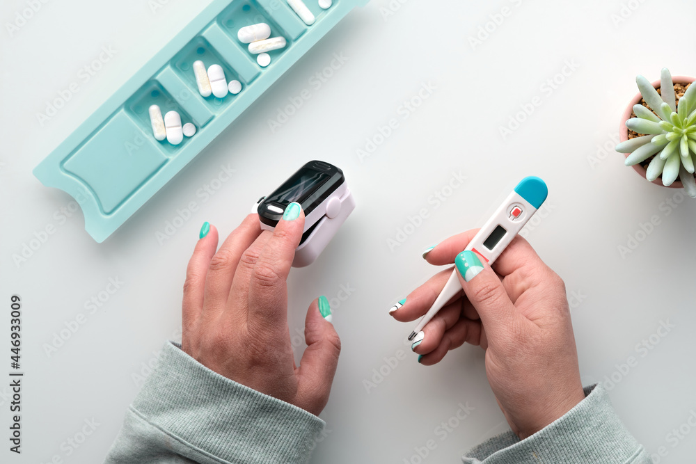 Patient hands with pills and pulse oximeter, finger digital device to measure oxygen saturation