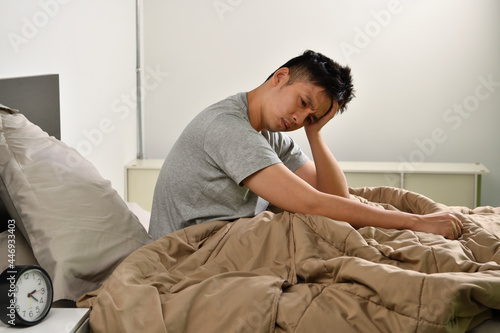 Depressed young Asian man sitting in bed cannot sleep from insomnia