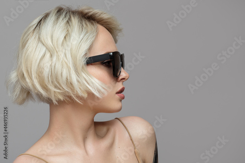 Portrait of a blonde girl with a short haircut in black sunglasses. Grey background.