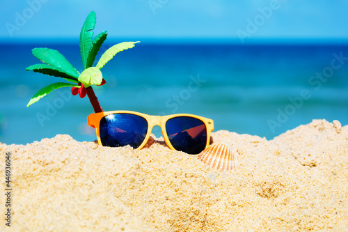 Kid's sunglasses and toy palm in sand on sea beach