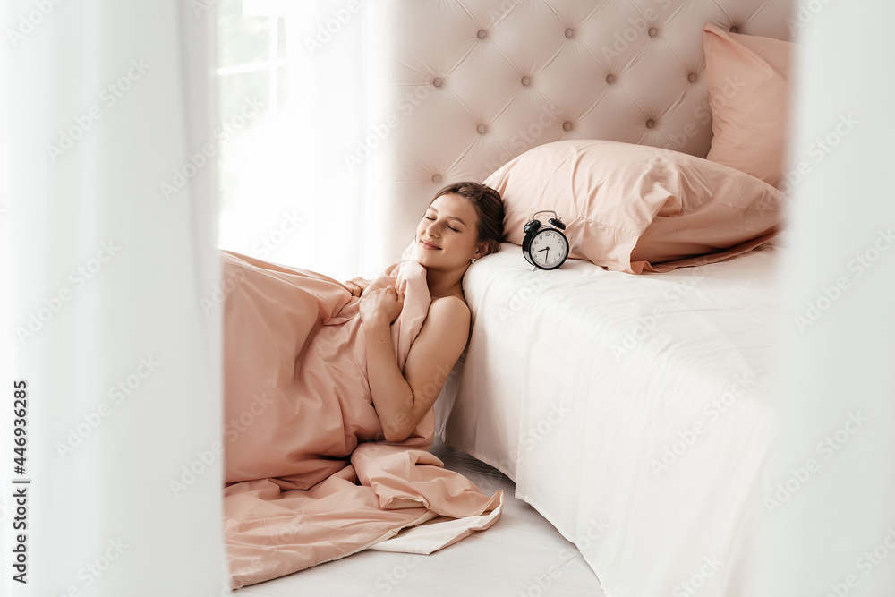 Young woman with alarmclock on the bed at the morning. Early wake up, not getting enough sleep, going work concept Young woman with alarmclock on the bed at the morning. Early wake up, not getting enough sleep, going work concept