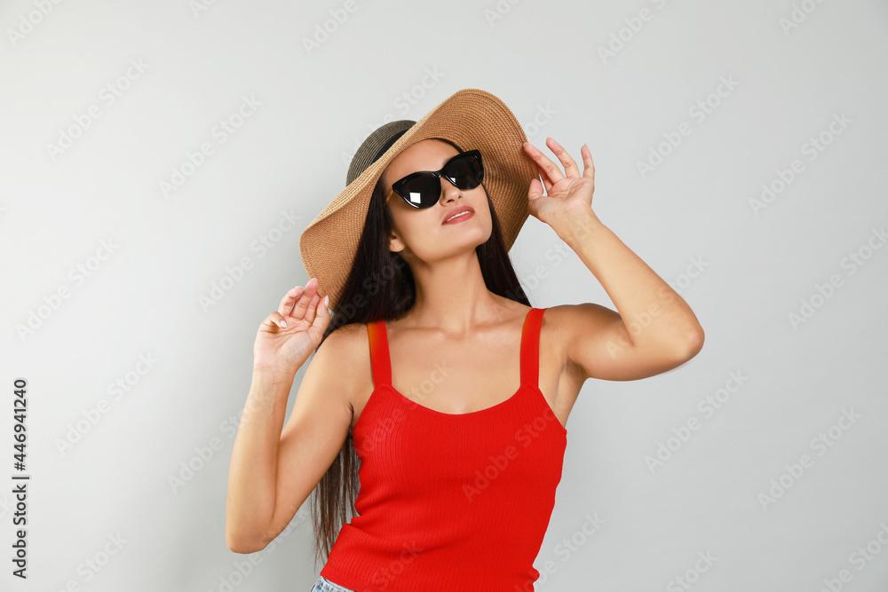 Beautiful young woman with straw hat and stylish sunglasses on light grey background Beautiful young woman with straw hat and stylish sunglasses on light grey background
