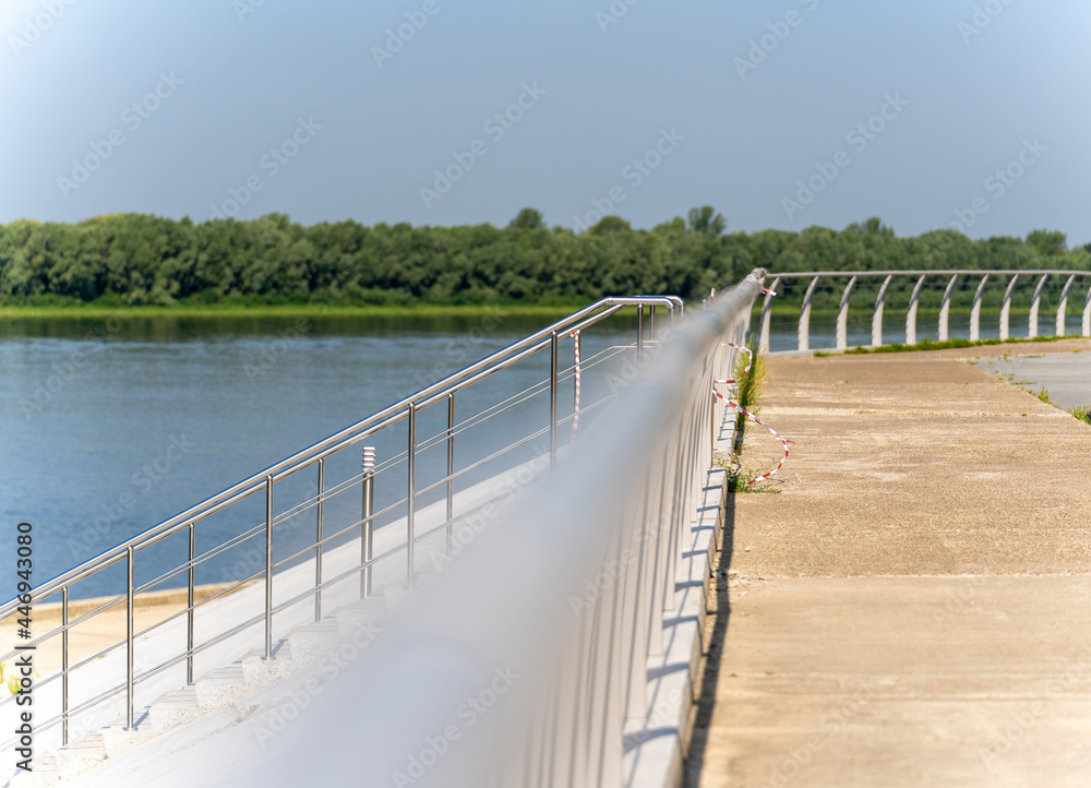 Metal, curved, horizontal fence, river embankment, the foreground is blurred