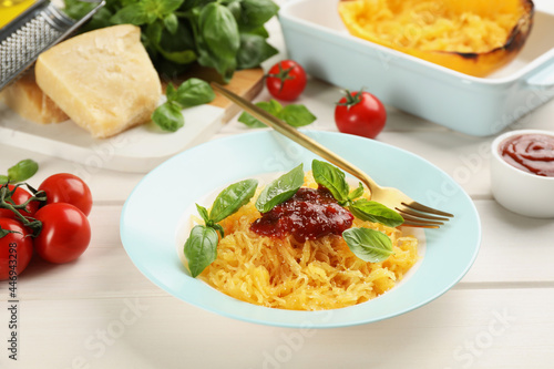 Tasty spaghetti squash with tomato sauce, cheese and basil served on white wooden table