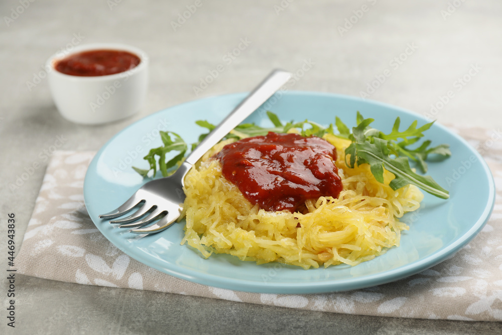 Tasty spaghetti squash with tomato sauce and arugula served on light grey table