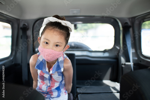 車の後部座席に座るマスクを着用した少女 photo