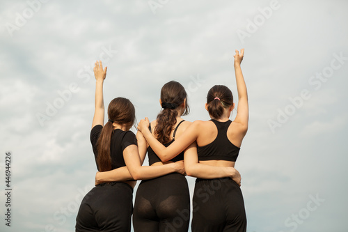three athletic young women with raised arms against the sky 