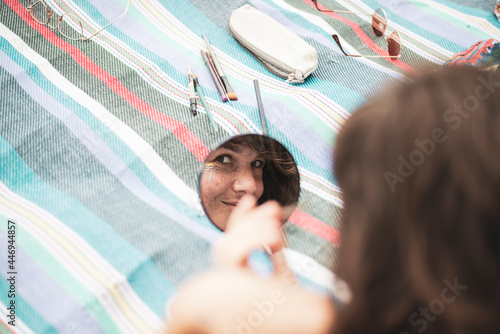 Artistic woman's reflection in mirror facepainting on summer blanket photo