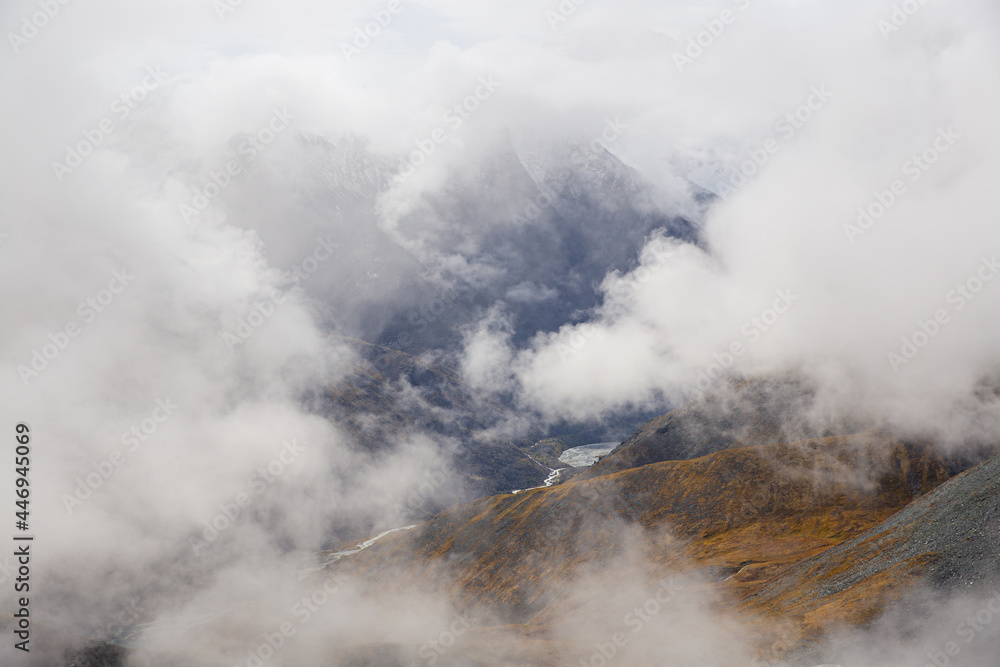 Clouds fly over the mountain valley. Mountain peaks between clouds. Photo from above. Soft focus. Selective focus on hills. Clouds fly over the mountain valley. Mountain peaks between clouds. Photo from above. Soft focus. Selective focus on hills.