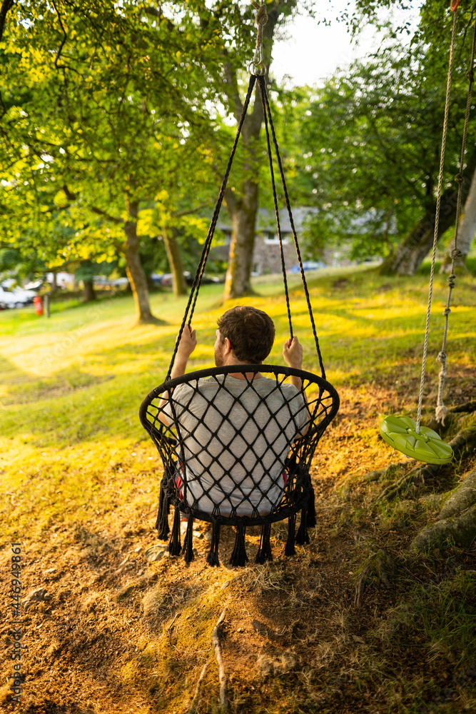 Photo of a attractive young guy relaxing on a hammock in the middle of nature. It is a summer day in the forest and he has a happy smile